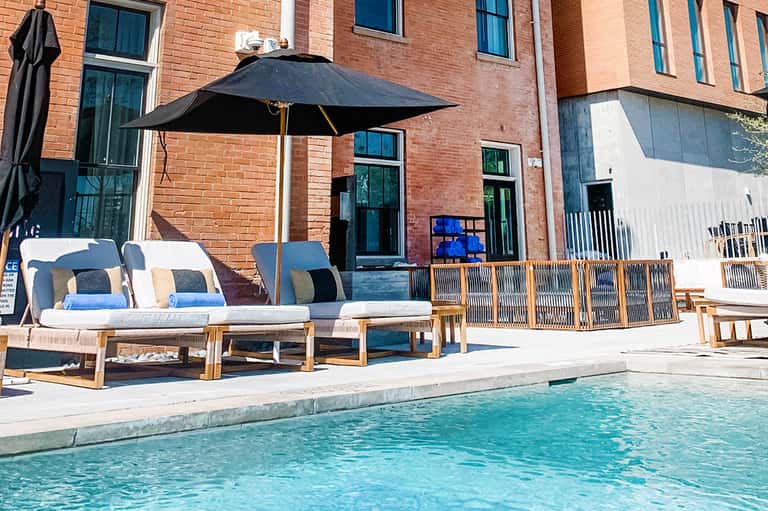 Modern pool deck with black umbrella, wooden lounge chairs, and brick building