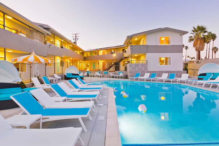 Resort pool area at dusk with blue loungers, illuminated buildings, and palm trees