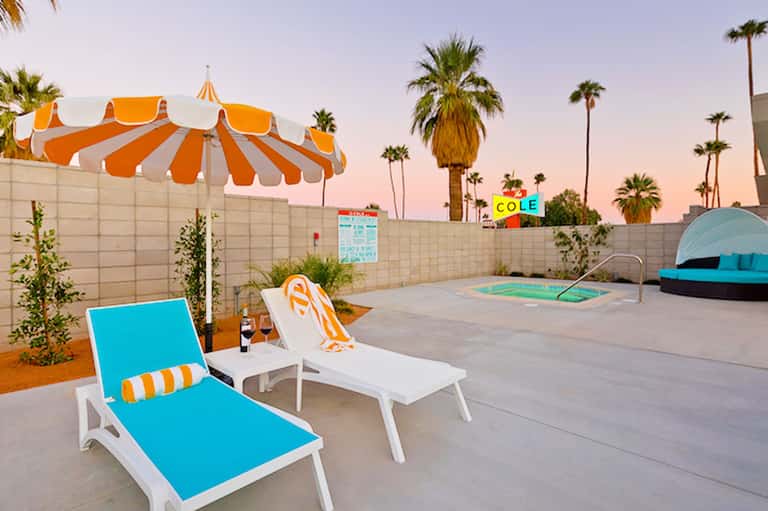Retro-style motel pool area with orange and white striped umbrellas and palm trees at dusk