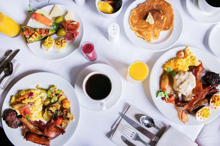Breakfast spread with eggs, bacon, pancakes, fresh fruit, coffee, and juice