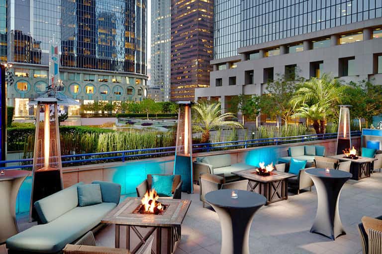 Rooftop lounge with fire pits, modern seating, and illuminated pool overlooking downtown city skyline