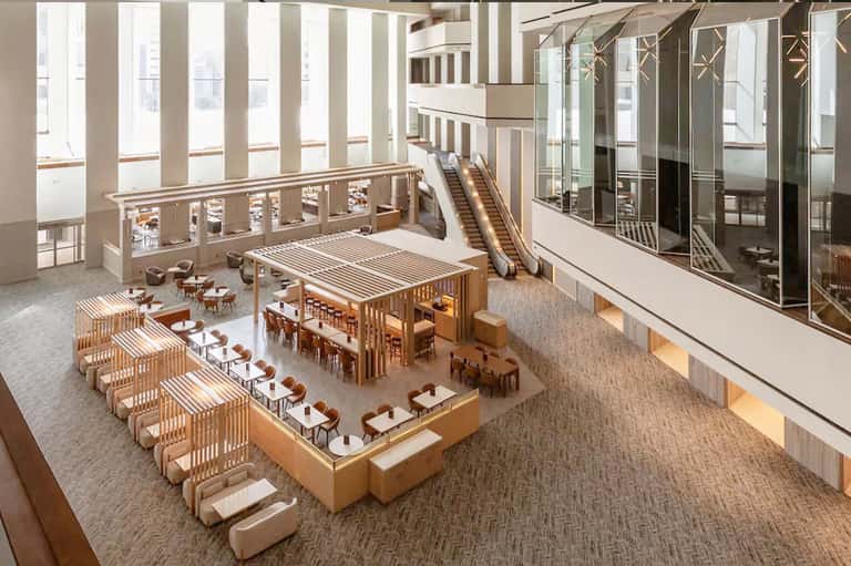 Modern hotel atrium with wooden furniture, escalators, and natural lighting from above