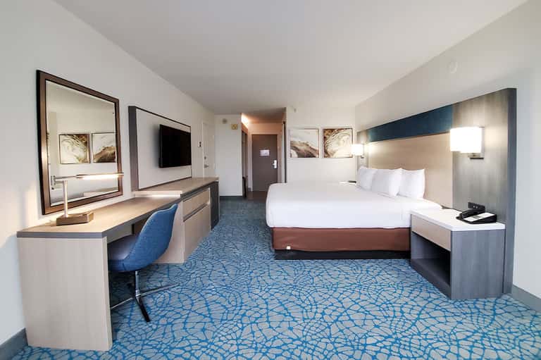 Modern hotel room with queen bed, work desk, flat-screen TV, and blue patterned carpet