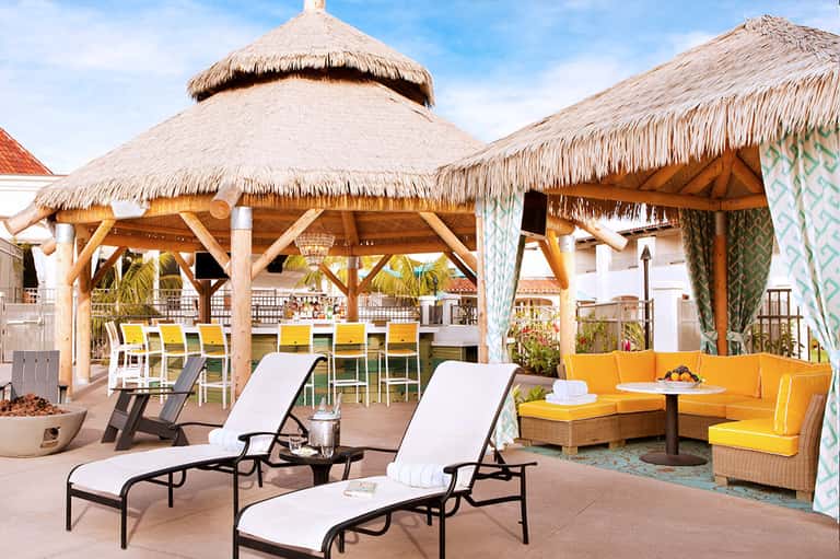 Beachfront resort patio with thatched-roof cabanas, yellow lounge chairs, and ocean views