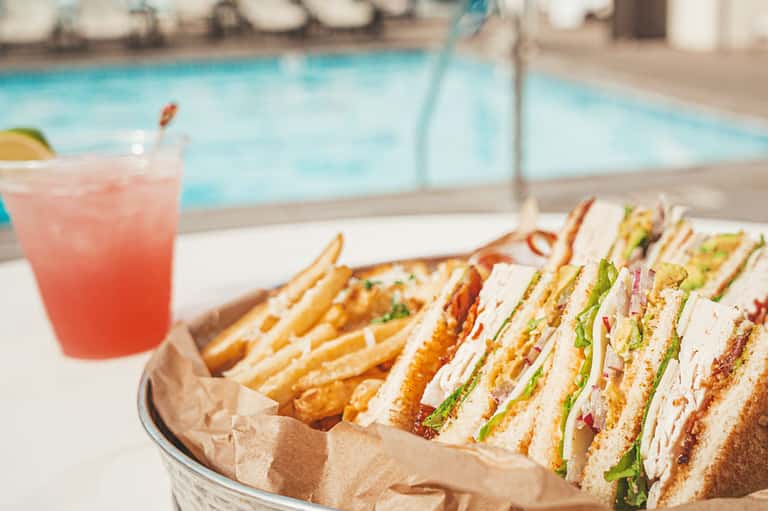 Poolside lunch spread with sandwiches, fries, and pink beverage