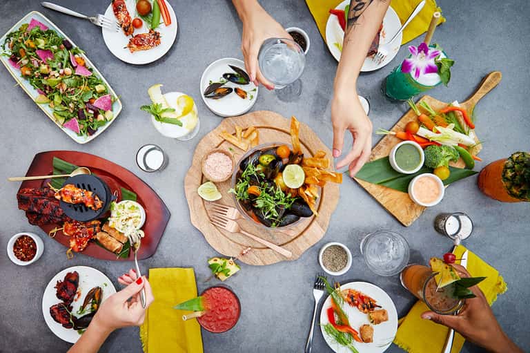 Overhead view of upscale dining with seafood, salads, and cocktails shared among multiple diners
