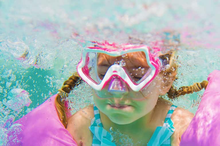 Child wearing colorful snorkel gear underwater in a swimming pool with vibrant water effects
