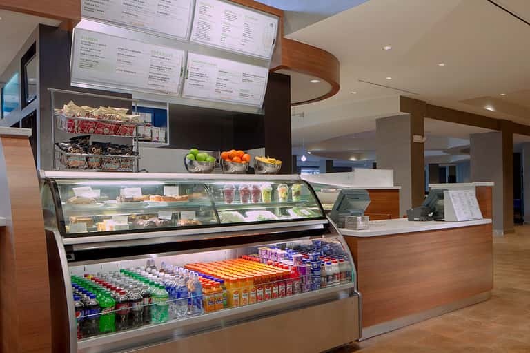 Modern cafe counter with refrigerated display cases, menu boards, fresh fruit, and beverages