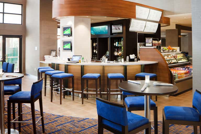 Modern hotel bar and lounge with wooden counter, blue seating, and full-service beverage station
