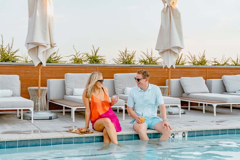 Couple sitting poolside enjoying drinks with umbrellas and comfortable loungers behind them