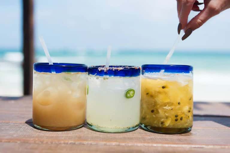 Three tropical cocktails with blue rim and straws on beach table