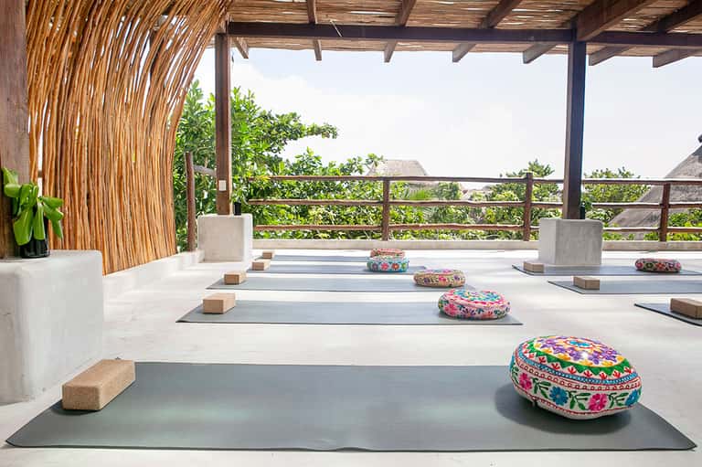 Yoga studio with wooden pergola, colorful meditation cushions, and mountain landscape views