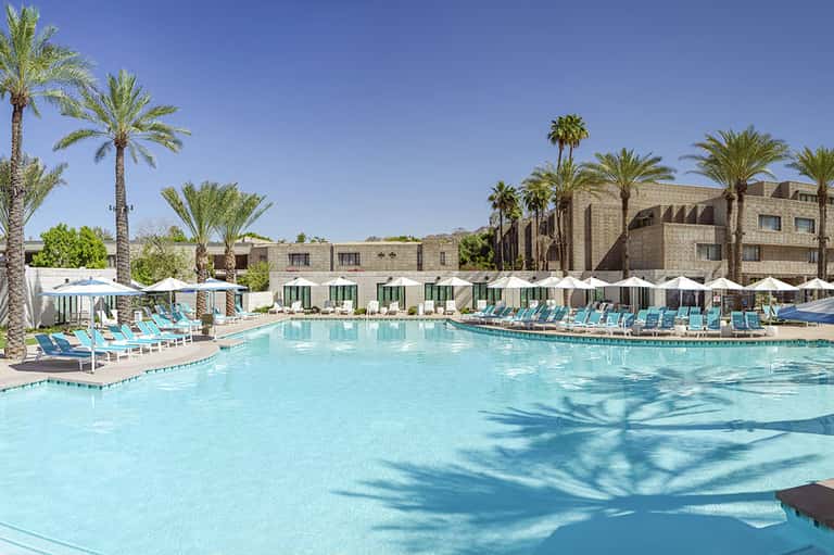 Resort pool with turquoise water, palm trees, and desert mountains
