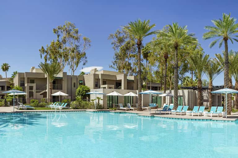 Resort courtyard with turquoise pool, modern concrete buildings, and palm trees
