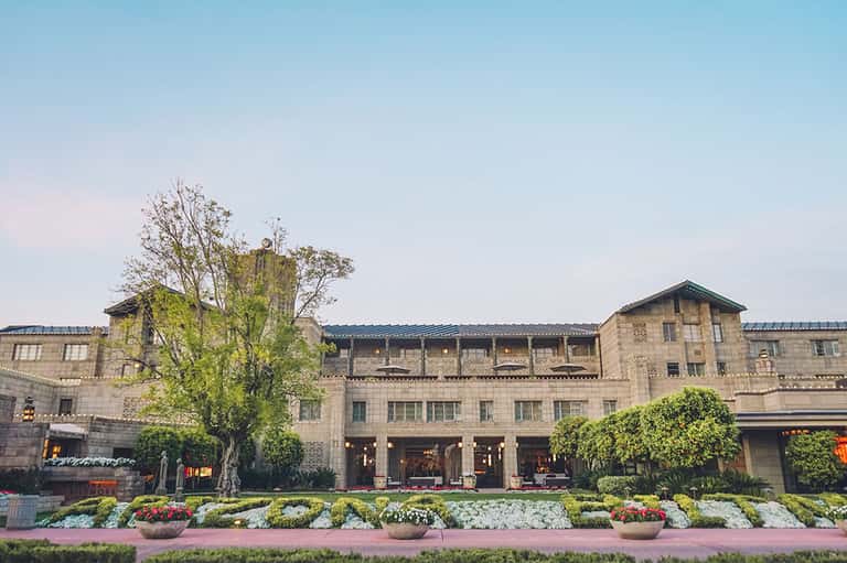Elegant stone hotel building with manicured gardens and flowering plants along the front entrance