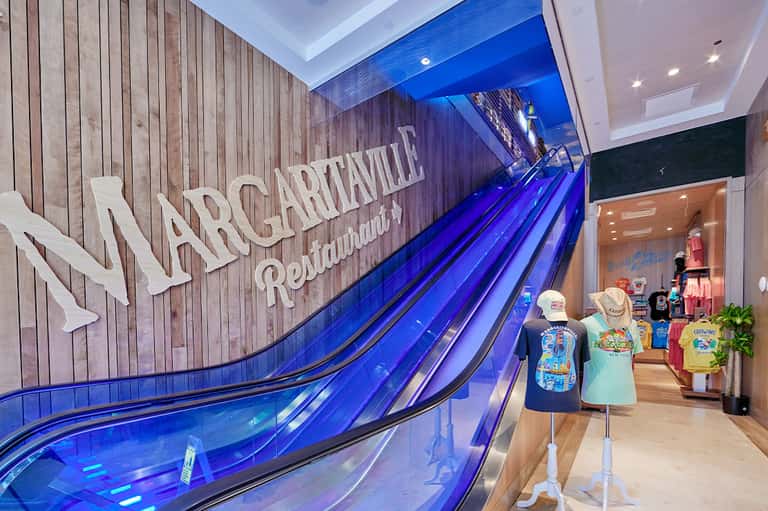 Modern escalators with Margaritaville signage and retail storefront in contemporary indoor mall setting