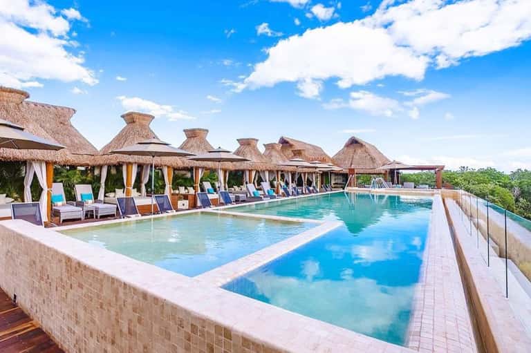 Luxury resort pool deck with thatched-roof cabanas, lounge chairs, and tropical landscape views