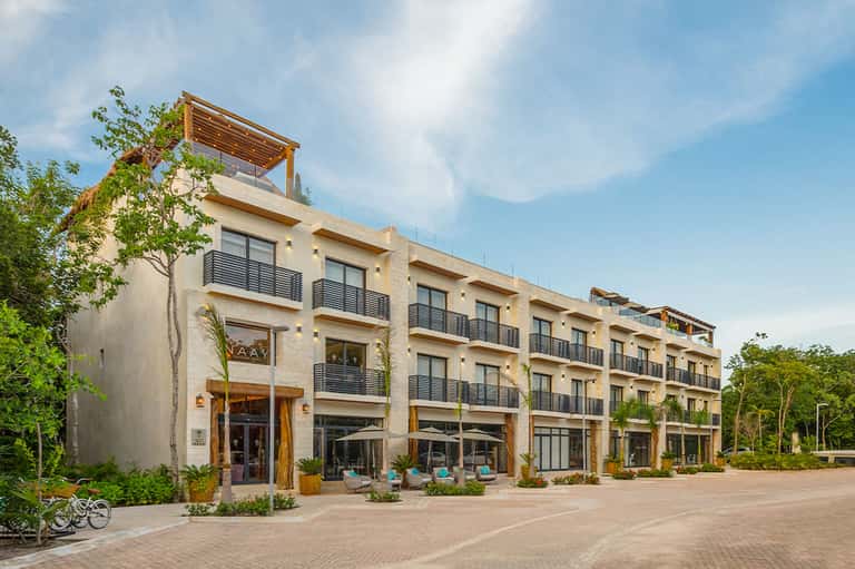 Modern beige residential building with multiple balconies, ground-floor retail spaces, and landscaped courtyard with seating areas
