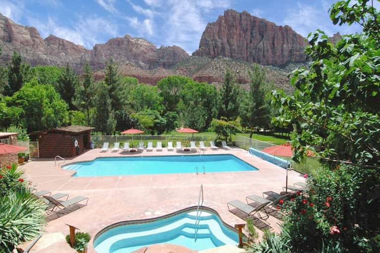 Resort pool with loungers and red umbrellas, mountain cliffs visible in background landscape