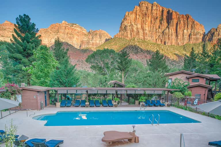 Resort swimming pool surrounded by blue lounge chairs with red rock canyon cliffs in background