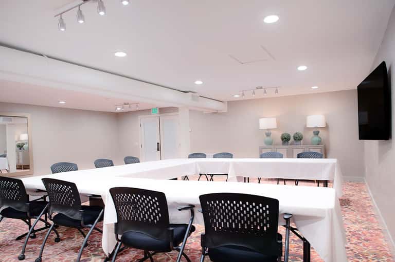 Modern conference room with U-shaped white table, black chairs, recessed lighting, and exit sign