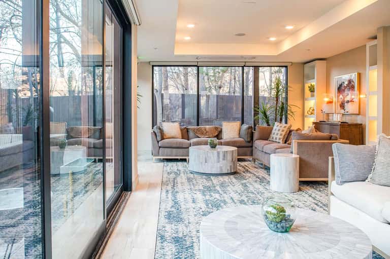 Contemporary living room with large windows, tan upholstered furniture, round marble coffee table, and natural light