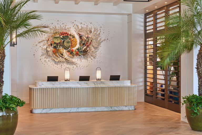 Modern hotel reception desk with marble countertop, wooden slats, decorative wall art, and potted plants