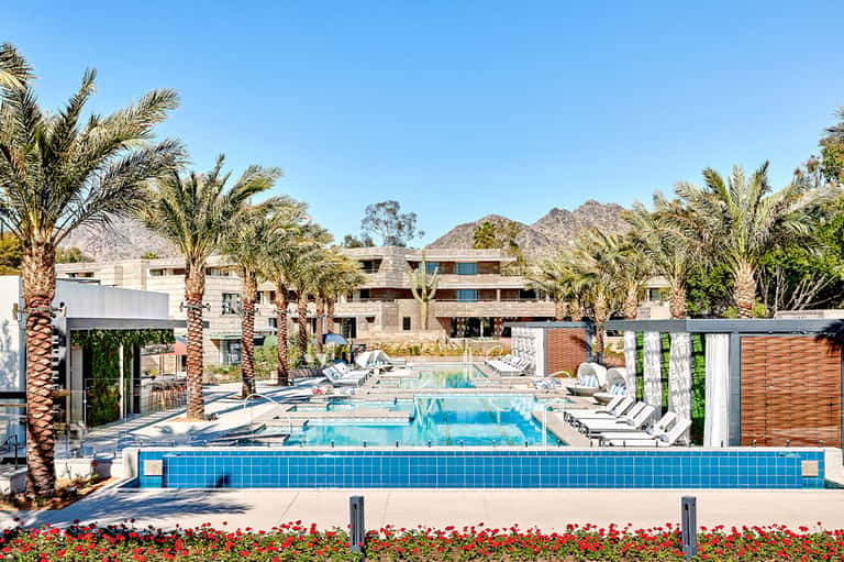 Resort pool complex with blue tiles, palm trees, and multi-story buildings against desert mountains