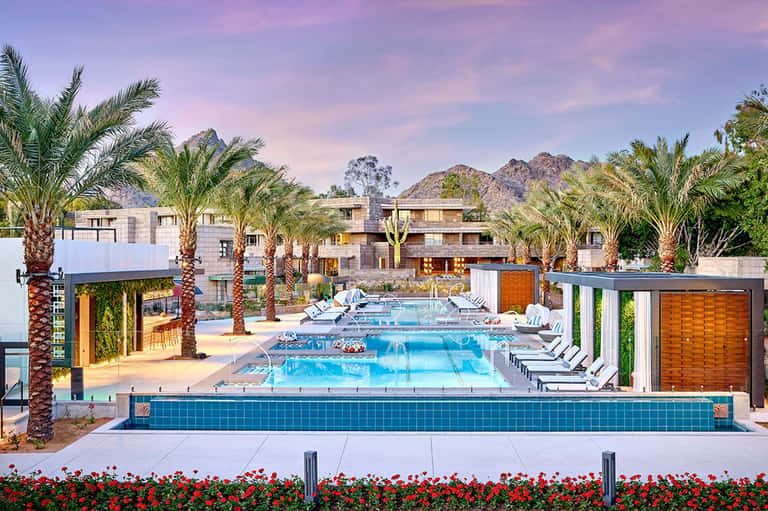 Resort pool area with palm trees, lounge chairs, and mountains in background at daytime