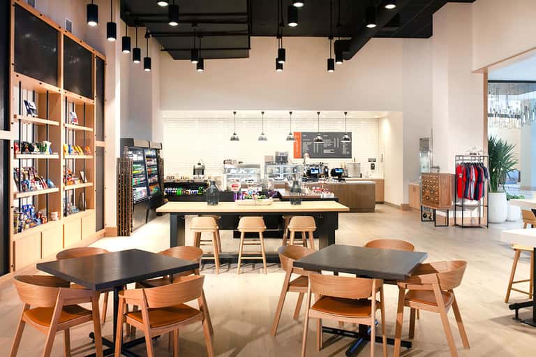 Modern resort café interior with wooden furnishings, shelving, pendant lighting, and service counter