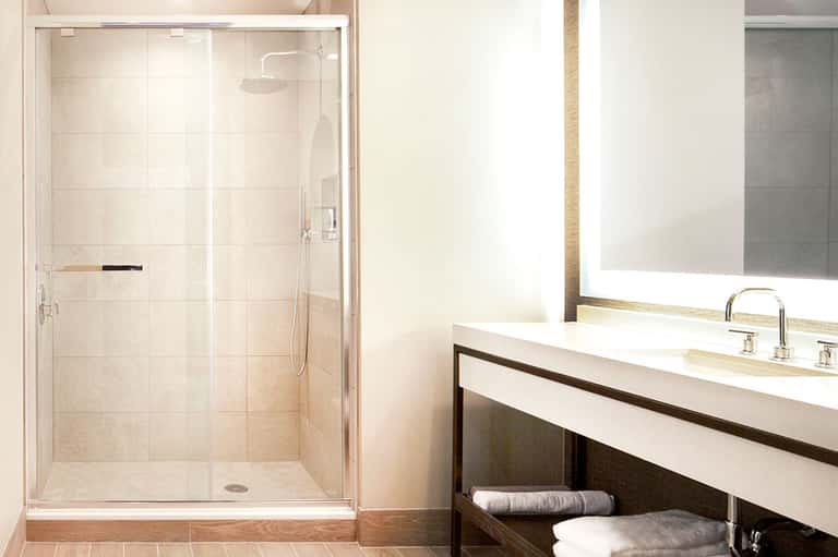 Modern bathroom with glass-enclosed shower, white vanity, mirror, and rolled towels