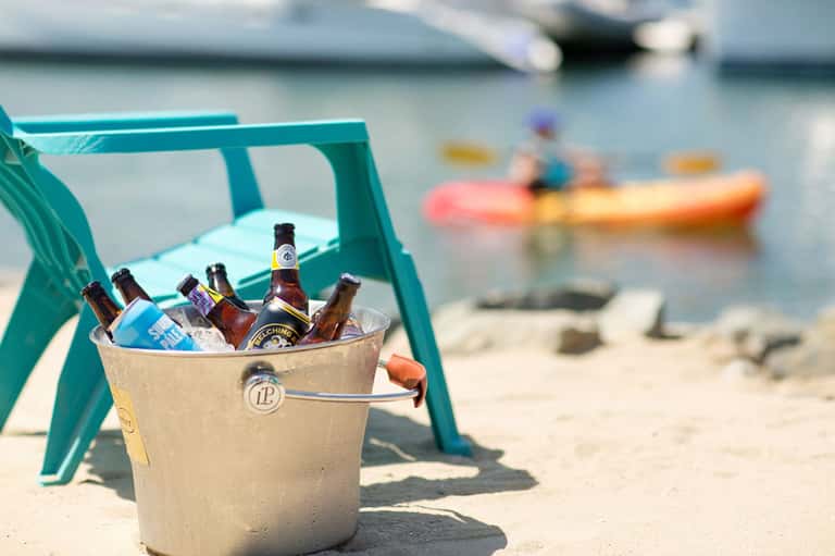 Bucket of cold beers on beach chair with kayakers and boats blurred in background