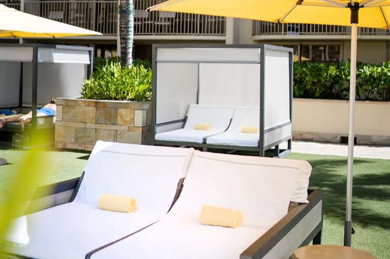 Luxury resort pool deck with white lounge chairs, yellow umbrellas, and cabanas on synthetic grass
