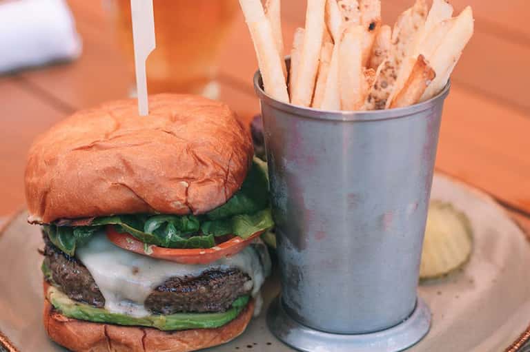 Gourmet burger with lettuce and tomato served with golden fries in metal cup