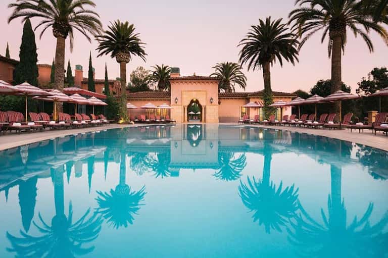 Luxurious resort pool surrounded by palm trees and pink loungers at dusk