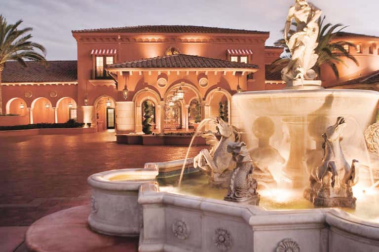 Illuminated Spanish colonial-style courtyard at dusk with ornate fountain and terracotta building facade