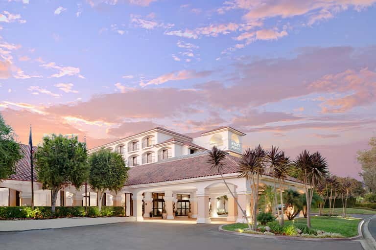 Luxury resort exterior at sunset with white columns, palm trees, and manicured grounds