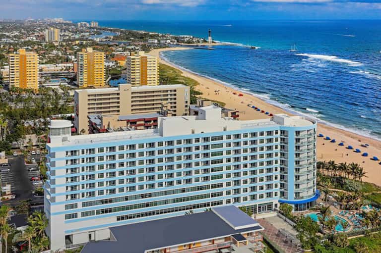 Aerial view of beachfront hotel tower with blue loungers on sandy beach and turquoise ocean