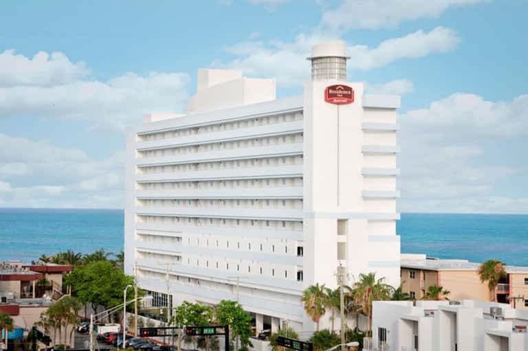 White multi-story beachfront hotel building with ocean view and palm trees