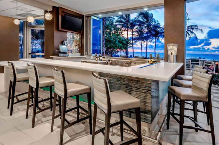 Luxury bar with ocean and palm tree views, bar seating, and tropical sunset backdrop