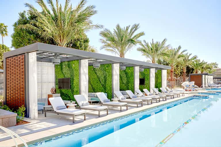 Modern pool cabanas with white columns and green living walls alongside lap pool