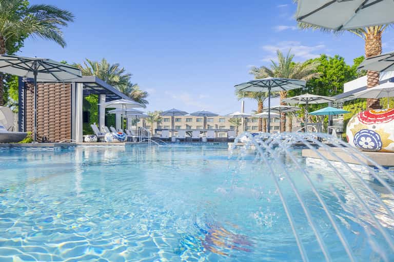 Resort swimming pool with loungers, umbrellas, and palm trees under blue sky