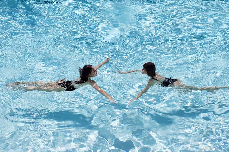 Two women swimming together in crystal clear turquoise pool water