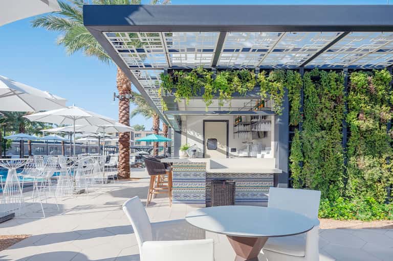 Modern outdoor bar with living green walls, white furniture, and covered pergola seating area