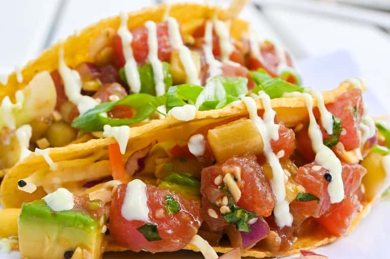 Gourmet fish tacos topped with white sauce, fresh toppings, and vibrant garnishes