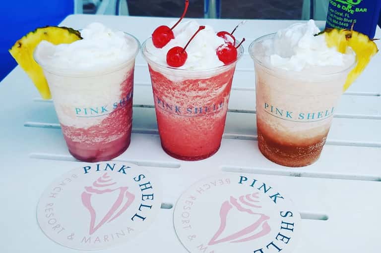 Three colorful layered cocktails with pineapple garnish at Pink Shell resort bar