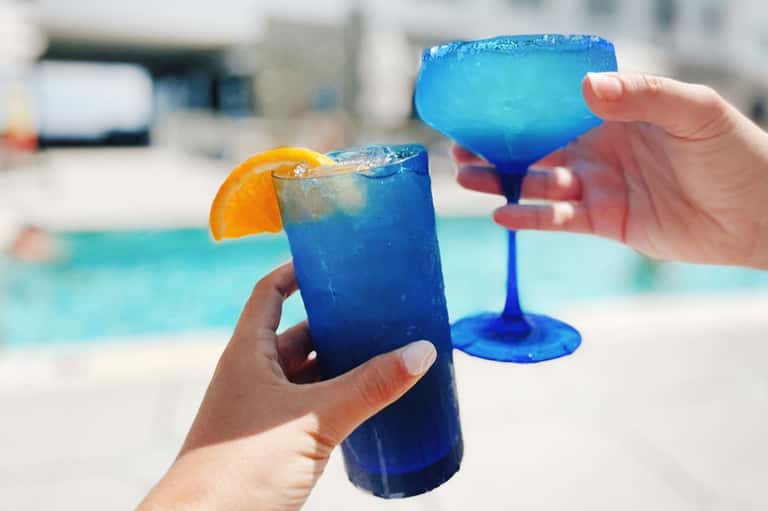 Vibrant blue cocktails by the pool with orange garnish and colorful frozen glasses