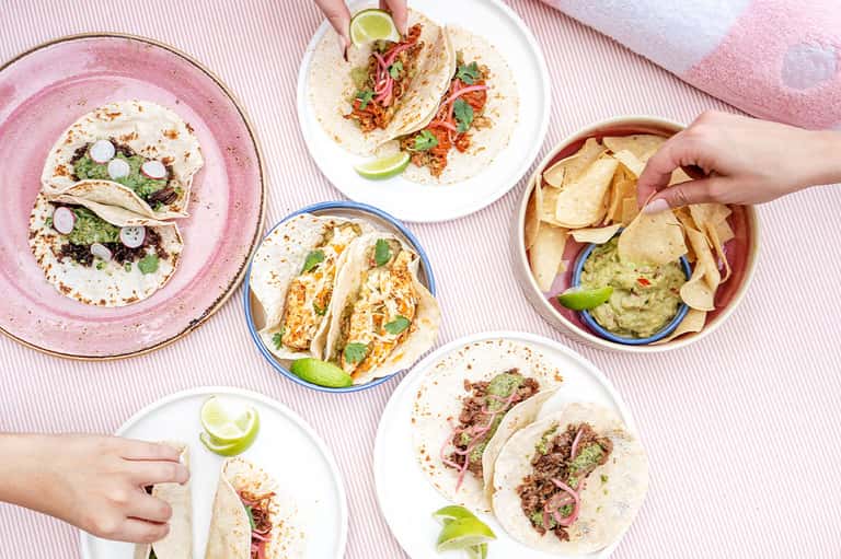 Assorted tacos and guacamole with tortilla chips on colorful plates with lime garnishes