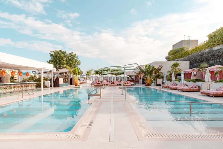 Luxury resort outdoor pool deck with lounge chairs, umbrellas, and pink cabanas under blue sky