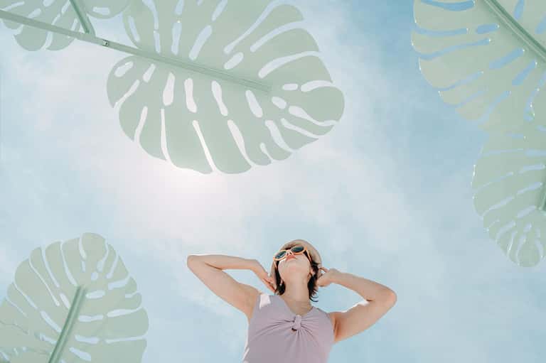 Woman in sunglasses relaxing under decorative monstera leaf ceiling panels against blue sky